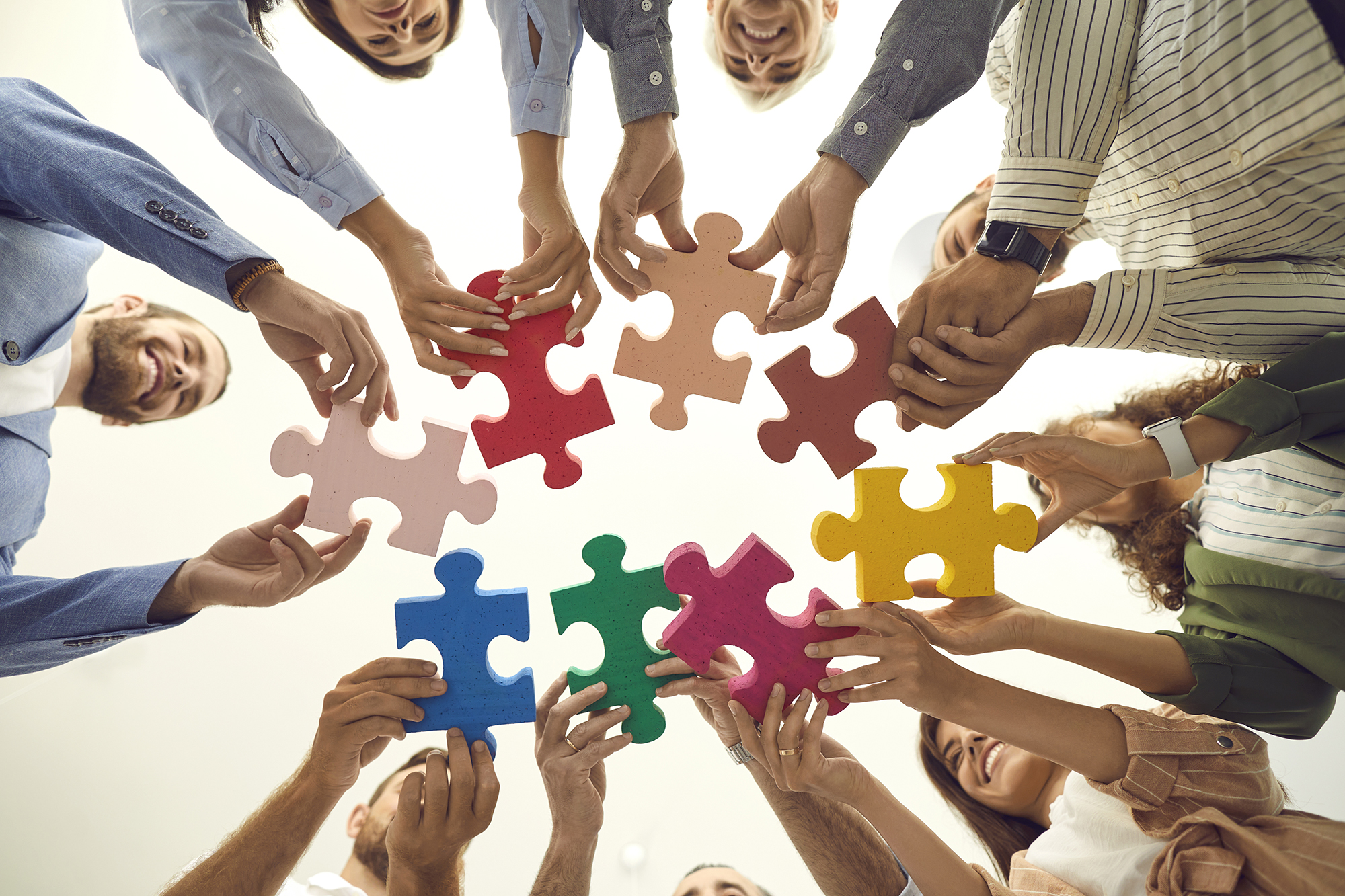 Shot from below of team of happy business people connecting pieces of jigsaw puzzle